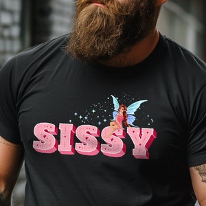 May include: A black t-shirt with a pink graphic of a fairy sitting on the word "Sissy".
