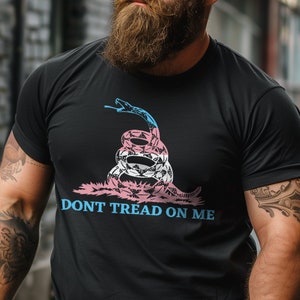 May include: A black t-shirt with a graphic of a snake with a transgender pride flag design. The text "DONT TREAD ON ME" is printed below the snake.