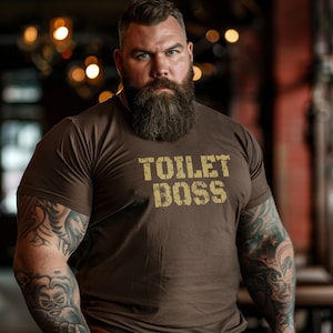 May include: A brown t-shirt with the text "TOILET BOSS" printed in a distressed gold font.