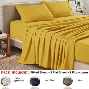 May include: A mustard yellow fitted sheet set with two pillowcases. The set includes a fitted sheet, a flat sheet, and two pillowcases. The set is available in a variety of colors, including silver, navy blue, white, grey, black, and sand.