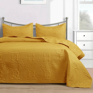 Puede incluir: Juego de colcha acolchada de color amarillo mostaza con dos fundas de almohada a juego. La ropa de cama presenta un patr&oacute;n circular detallado y repetitivo. La cama est&aacute; hecha con el juego y el cabecero es plateado.