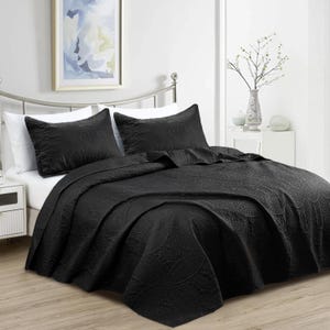 Puede incluir: Un edred&oacute;n negro y dos fundas de almohada a juego con un estampado floral. La ropa de cama se exhibe en una cama con estructura met&aacute;lica. Una imagen enmarcada cuelga de la pared sobre la cama.
