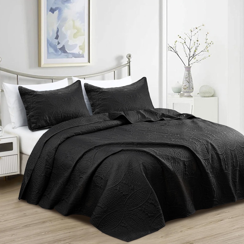 Puede incluir: Un edred&oacute;n negro y dos fundas de almohada a juego con un estampado floral. La ropa de cama se exhibe en una cama con estructura met&aacute;lica. Una imagen enmarcada cuelga de la pared sobre la cama.