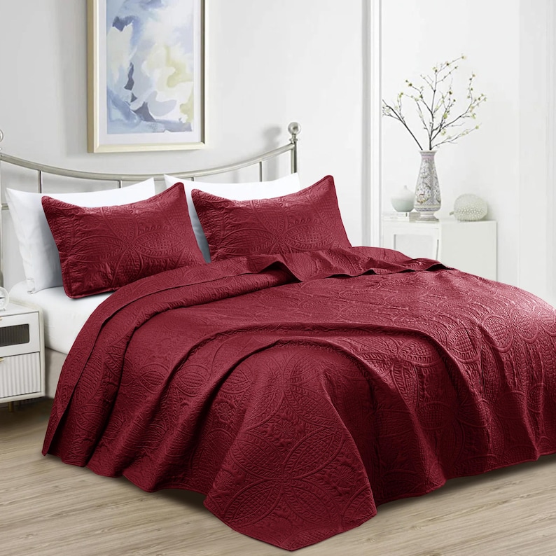 Puede incluir: Un juego de colcha burdeos con dos fundas de almohada a juego. La ropa de cama presenta un patr&oacute;n floral en relieve detallado. La cama est&aacute; hecha con s&aacute;banas blancas y una estructura de cama de metal plateado.