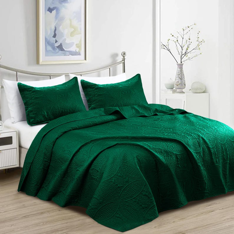 Puede incluir: Una cama est&aacute; hecha con una colcha acolchada verde oscuro y dos fundas de almohada a juego. La ropa de cama tiene un estampado de cachemira texturizado. La cama est&aacute; hecha con s&aacute;banas blancas y est&aacute; contra una pared blanca con una imagen enmarcada.