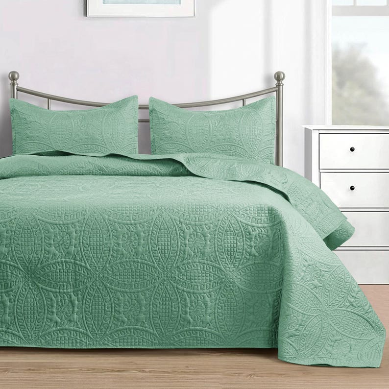 Puede incluir: Un juego de colcha verde menta con dos fundas de almohada a juego. La ropa de cama presenta un patr&oacute;n floral y geom&eacute;trico en relieve detallado. La cama est&aacute; hecha con la colcha y las fundas de almohada, lista para usar.