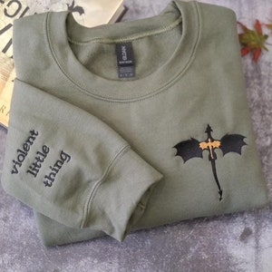May include: A green sweatshirt with a black embroidered dragon on the front and the words "violent little thing" embroidered on one sleeve.