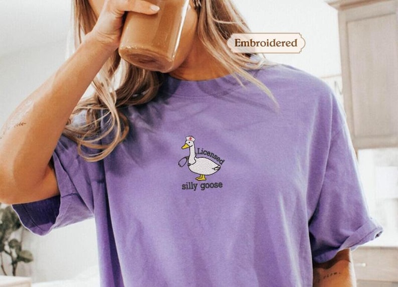 A person wearing a purple t-shirt with a cartoon goose and the text "silly goose" printed on it.