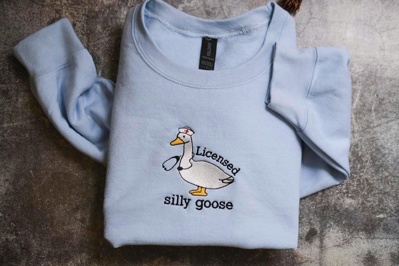 A light blue t-shirt with a cartoon image of a duck wearing a nurse's hat and the text "Licensed silly goose" printed on it.