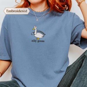 A person wearing a blue t-shirt with a cartoon goose and the text "licenced silly goose" embroidered on it.