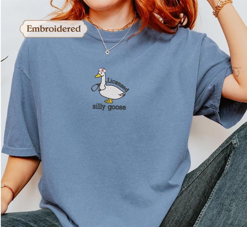 A person wearing a blue t-shirt with a cartoon goose and the text "licenced silly goose" embroidered on it.