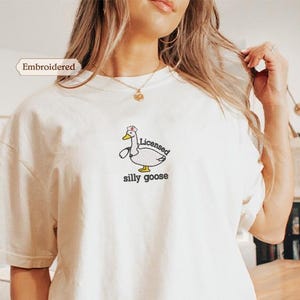 A woman wearing a white t-shirt with a cartoon duck and the text "Licensed silly goose" printed on it.