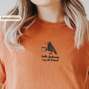 a person wearing an orange t-shirt with a black bird embroidered on it.