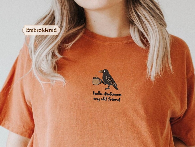 a person wearing an orange t-shirt with a black bird embroidered on it.