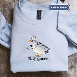 A light blue t-shirt with a cartoon image of a duck wearing a nurse's cap and the text "Licenced silly goose" printed on it.
