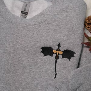 a gray sweater with a bat embroidered on it