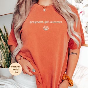 a woman wearing an orange shirt with the words pregnant girl summer on it