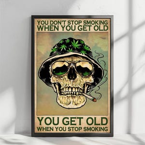 May include: Framed poster with a skull wearing sunglasses and a hat adorned with cannabis leaves, smoking a cigarette. The poster has the text "YOU DON'T STOP SMOKING WHEN YOU GET OLD" at the top and "YOU GET OLD WHEN YOU STOP SMOKING" at the bottom.