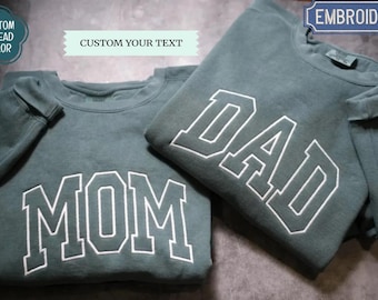 May include: Two teal sweatshirts with white embroidered lettering. One says "MOM" and the other says "DAD". The sweatshirts have a crew neck and long sleeves. The image also includes text that says "CUSTOM THREAD COLOR", "CUSTOM YOUR TEXT", and "EMBROIDERY".