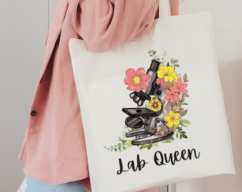 May include: White canvas tote bag featuring a floral design and a microscope. The text "Lab Queen" is printed on the bag.