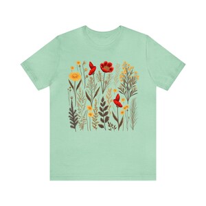 May include: A light green t-shirt with a floral print featuring red poppies and yellow flowers. The print is a botanical illustration style.
