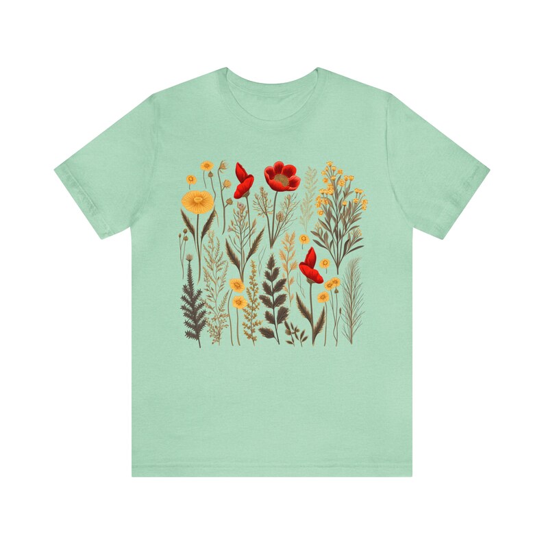 May include: A light green t-shirt with a floral print featuring red poppies and yellow flowers. The print is a botanical illustration style.