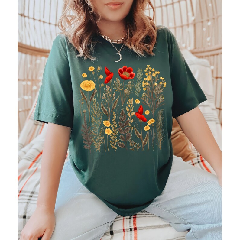 May include: A dark green t-shirt with a floral print featuring red and yellow flowers. The flowers are arranged in a cluster and are surrounded by green leaves.