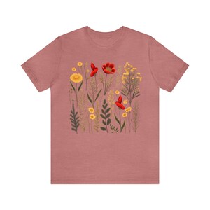 May include: A mauve t-shirt with a floral print featuring red poppies and yellow wildflowers.