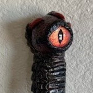 May include: A wooden walking stick with a detailed dragon head handle. The handle is painted red and black with a large, red eye.