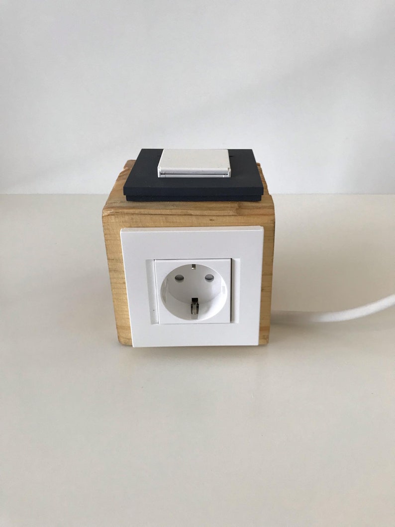 May include: A wooden box with a white electrical outlet and a black light switch on top. The box is sitting on a white surface.