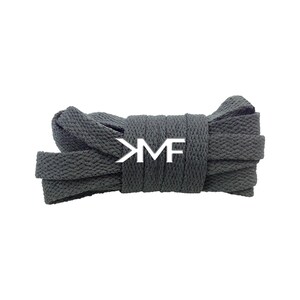 May include: Dark gray flat shoelaces, neatly coiled. The laces have a textured appearance and a white logo that reads "KM". The shoelaces are against a white background.