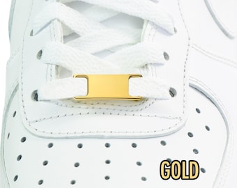 May include: Close-up of a white leather trainer with white laces and a gold-coloured lace lock. The word "GOLD" is printed in a yellow outline on the shoe.