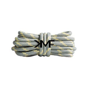 May include: A bundle of gray and yellow rope with the letters "KM" in black. The rope is tightly coiled and appears to be new. The rope has a pattern of yellow flecks throughout the gray strands.