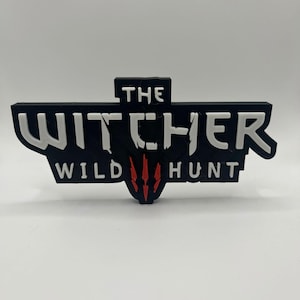 Pode incluir: Logotipo impresso em 3D em preto e branco de "The Witcher Wild Hunt" com um símbolo de cabeça de lobo vermelho.