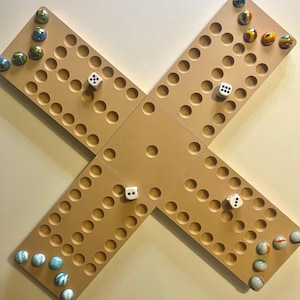 May include: A tan wooden game board in a cross shape, featuring circular indentations and colourful marbles. Four white dice are placed on the board. The marbles are various colours.