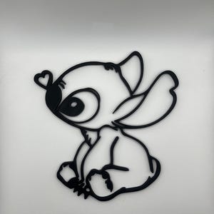 Op de afbeelding: Zwarte omtrek van het stripfiguur Stitch, met een hartvormig detail op het oor. Het personage zit, met grote ogen en een vriendelijke uitdrukking. De afbeelding is een eenvoudig, strak ontwerp.