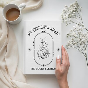 Peut inclure: Un journal blanc avec le texte "MY THOUGHTS ABOUT THE BOOKS I'VE READ" et une illustration de livres et de fleurs. Une tasse blanche avec du caf&eacute; et des fleurs blanches sont &eacute;galement visibles.
