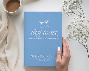 Könnte beinhalten: Ein hellblaues Buch mit dem Text "last toast on the coast" und zwei Cocktailgläsern. Das Buch enthält auch den Text "Olivia's Bachelorette" und das Datum 10. März 2026. Eine weiße Kaffeetasse und Blumen sind im Hintergrund.