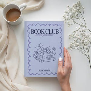 May include: A lilac-coloured "Book Club notes journal" with a floral illustration and the name "Jessica Smith." The journal is held by a person's hand, next to a cup of coffee and white flowers.
