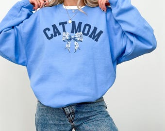 May include: A light blue sweatshirt with the text "CAT MOM" in navy blue letters and a floral bow design.