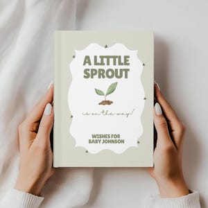 Op de afbeelding: Een boek met een lichtgroene kaft, vastgehouden door handen. De kaft toont de tekst "A LITTLE SPROUT is on the way!" in groen, met een spruitillustratie. Daaronder staat "WISHES FOR BABY JOHNSON."