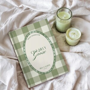 Peut inclure: Un livre à couverture rigide avec un motif vichy vert et blanc. La couverture porte l'inscription "Sweet Wishes For One Silly Goose" dans un cadre ovale décoratif. Une bougie verte dans un bocal en verre et une petite tasse de matcha sont également visibles.
