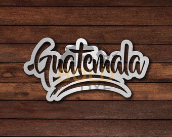 May include: A metal sign with the word "Guatemala" written in a stylized font. The sign is on a wooden background.