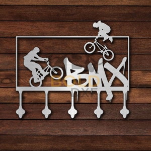 May include: Metal wall hook with five hooks shaped like dripping paint. The hooks are attached to a metal plate with a silhouette of three people riding BMX bikes and the word "BMX" in graffiti style.
