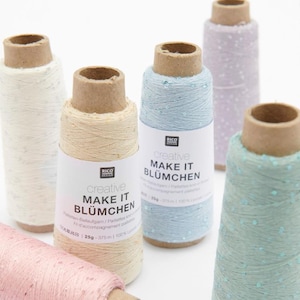 Könnte beinhalten: Verschiedene Garnrollen in Pastellfarben wie Rosa, Blau und Creme sind auf einer weißen Oberfläche angeordnet. Jede Rolle hat einen Pappkern und ein Etikett mit der Aufschrift "creative MAKE IT BLÜMCHEN". Das Garn scheint mit Pailletten verziert zu sein.