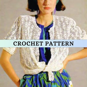 Puede incluir: Un cárdigan de crochet blanco con un delicado patrón de calado. El cárdigan está atado a la cintura y tiene mangas cortas.