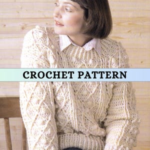 Può includere: Un maglione all'uncinetto color crema con un motivo strutturato e maniche lunghe. Il maglione presenta un design a rombi e pallini. Il testo "CROCHET PATTERN" è visualizzato su uno striscione azzurro. La donna indossa una camicia bianca con colletto sotto.