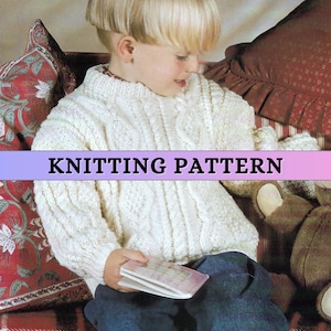 May include: A cream cable-knit sweater with a high collar. The sweater is worn by a child. The image has the text "KNITTING PATTERN" in a purple banner across the bottom. The child is holding a small book.