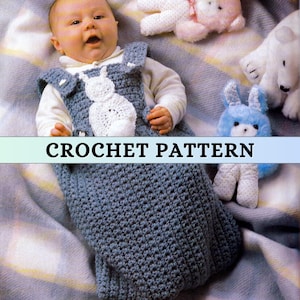Può includere: Un bambino indossa un sacco nanna all'uncinetto blu con un motivo a coniglietto bianco. L'immagine include il testo "CROCHET PATTERN". Il bambino è sdraiato su una coperta con peluche.