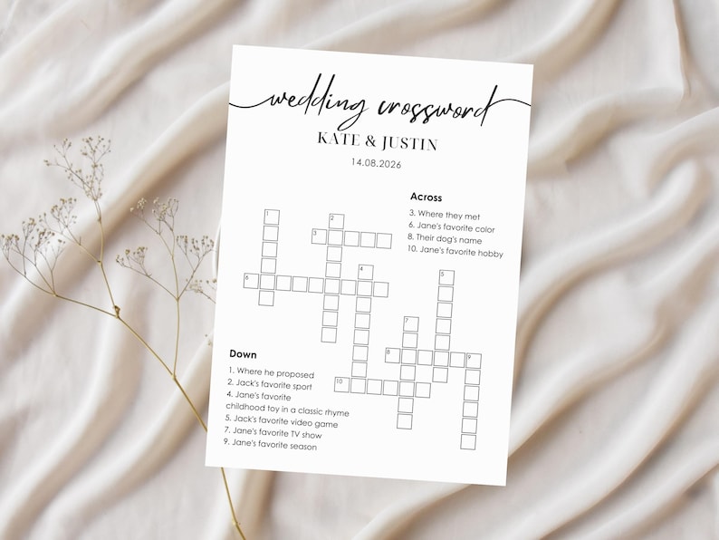 Wedding crossword puzzle card on white linen background with dried baby's breath flowers, minimalist black script "wedding crossword" header, couple names and personalized clues